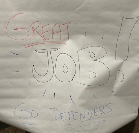 A poster reads "Great Job! Go Defenders" in red, black, and blue