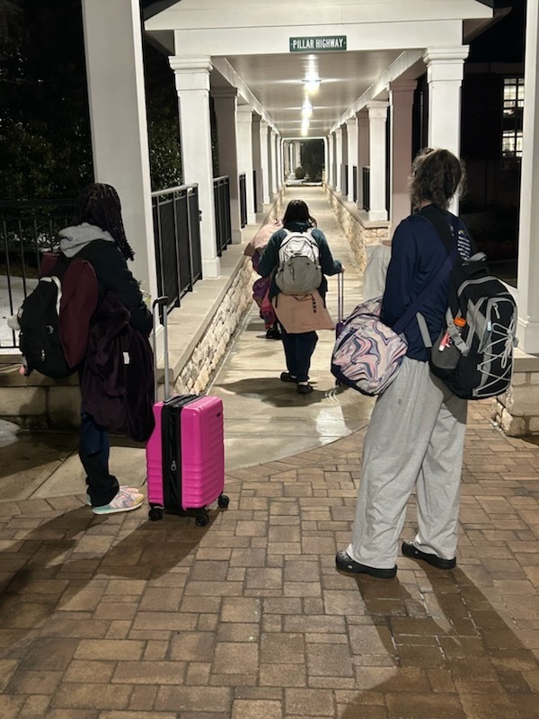Three students begin to walk down a pathway with their belongings