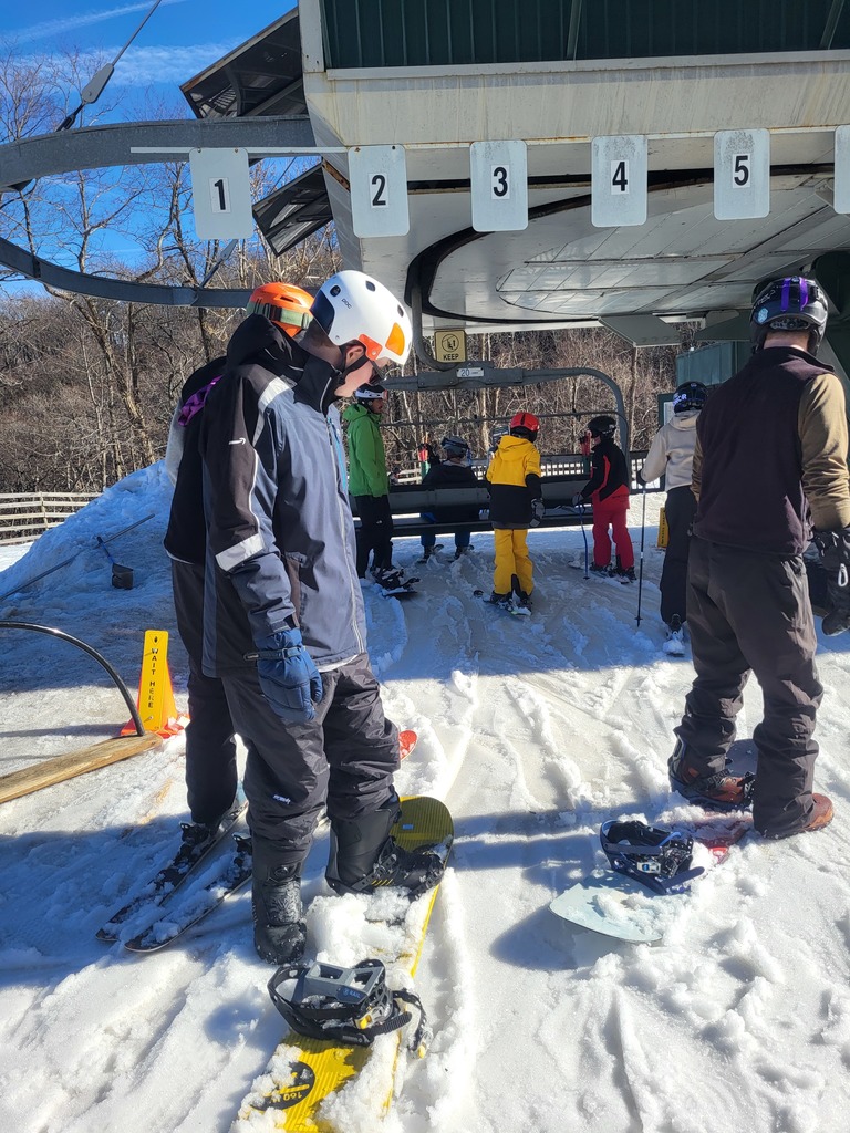 A blind snowboarder is preparing to get on the lift.