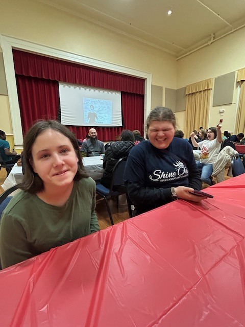 two female students sitting together at a table. one is smiling and one is laughing