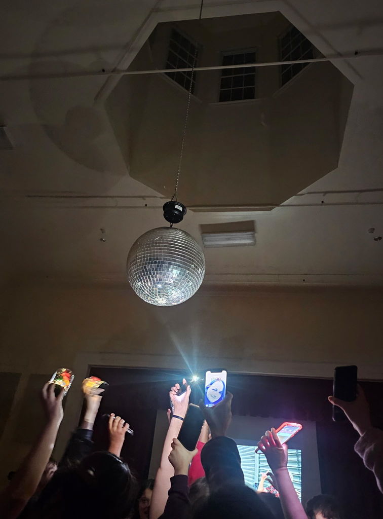 students and staff holding phone flashlights at a disco ball to see the light reflect around the room