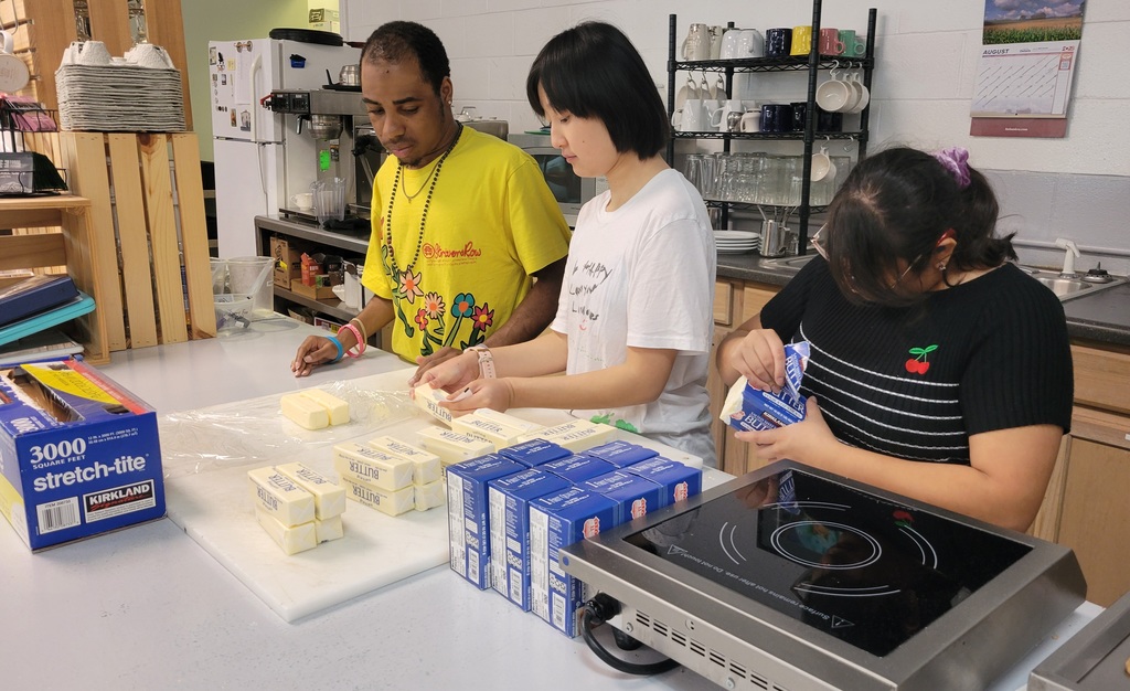 Three students are working with butter at a counter in a bakery.