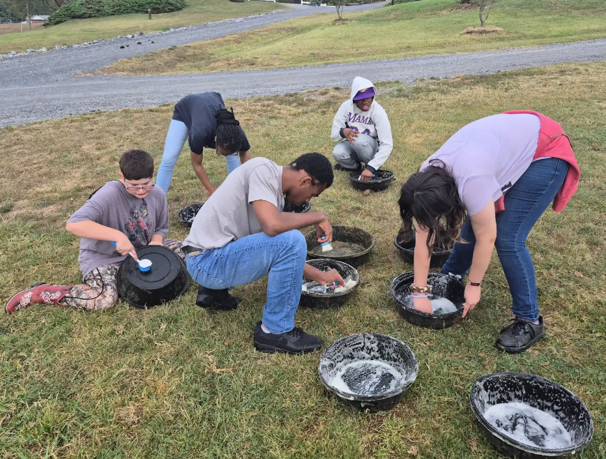 Students are washing platisc conatriners outside on the grass.