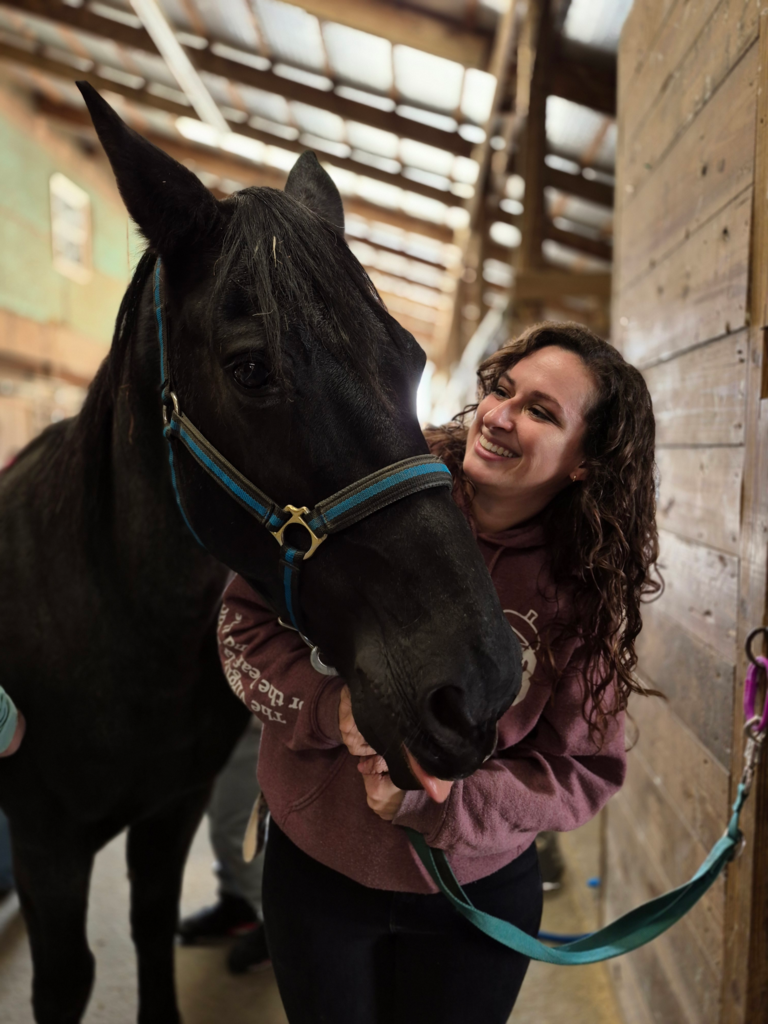 A teacher smiles at a black horse standing beside her.