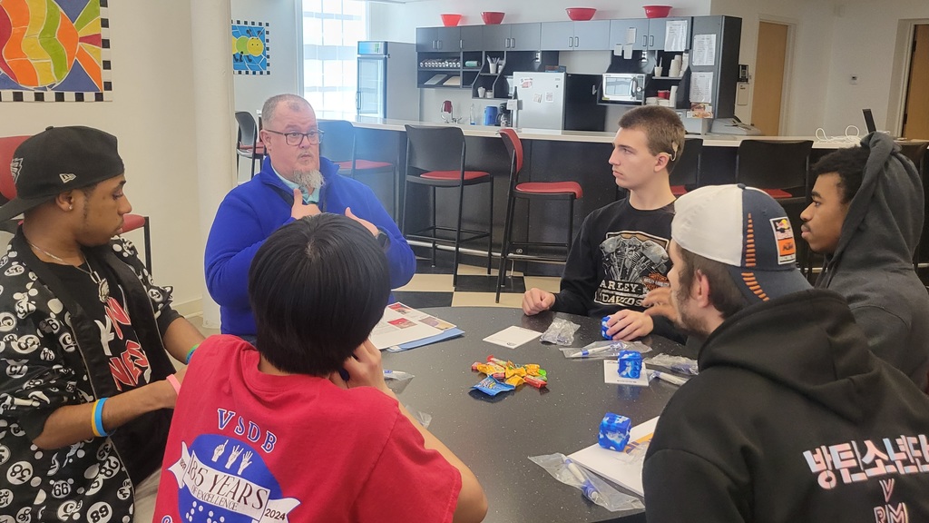 Students sit around a table looking at a speaker
