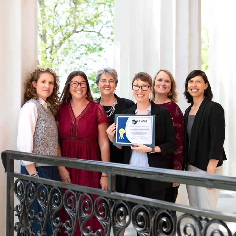 six women standing on the porch of main hall. one is holding the CEASD certificate