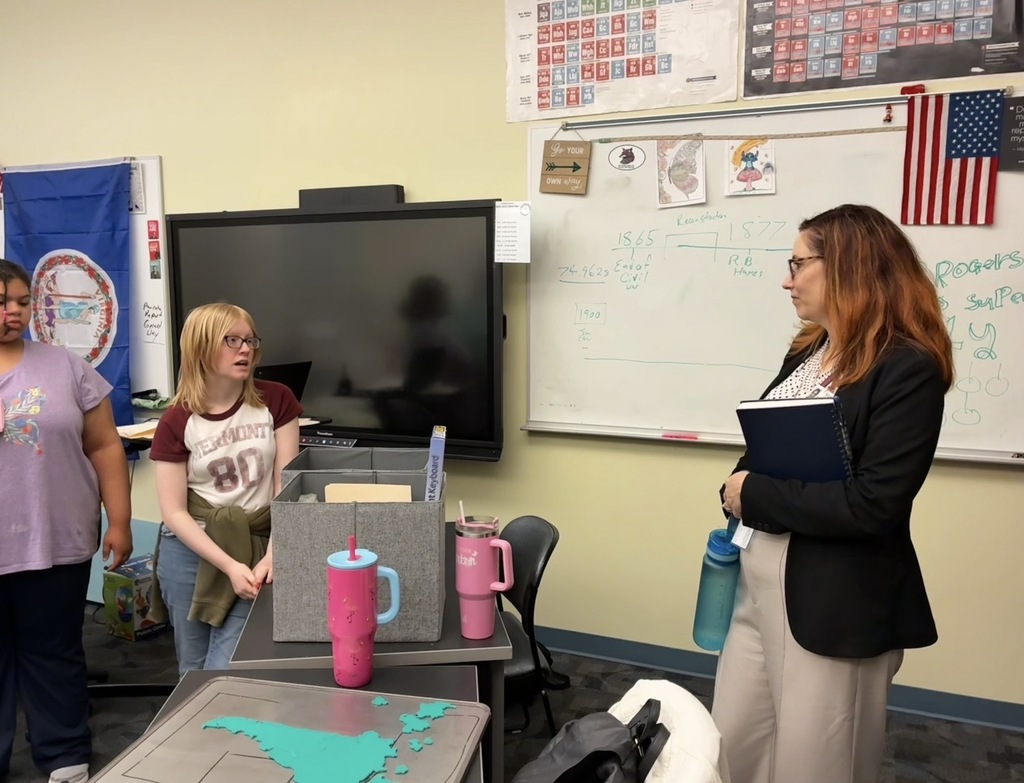 two female students talking to Dr. Maxlow in a classroom