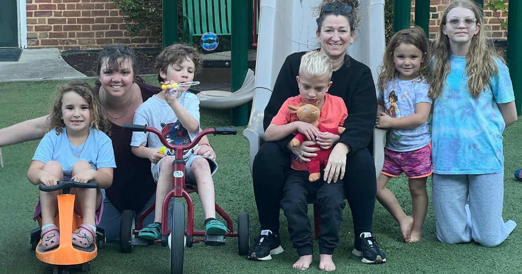 group of two staff, 4 children, and one teen helper on the playground, lined up and smiling for the camera
