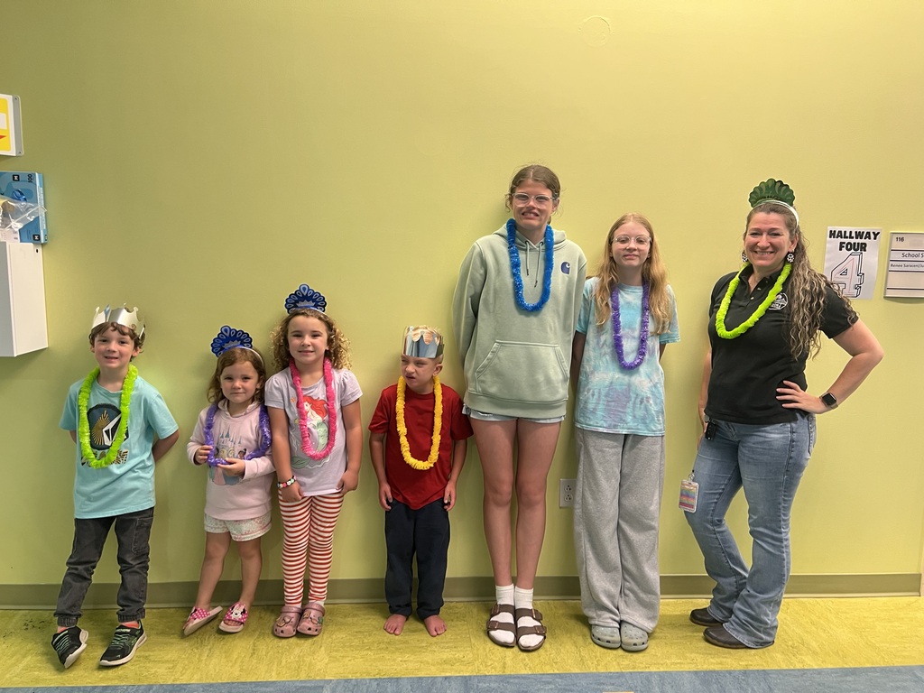 one staff, two teen helpers, and four children lined up against the wall and smiling for the camera. they are wearing leis and crowns. 