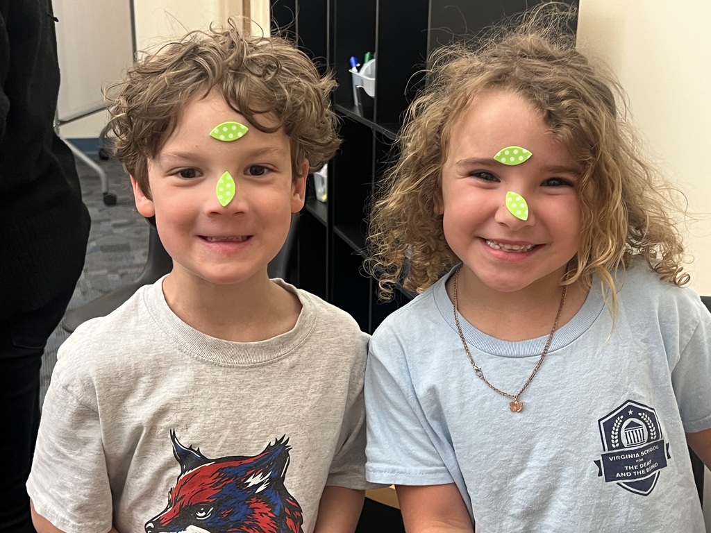 young boy and girl with curly hair and stickers stuck to their faces smiling for the camera
