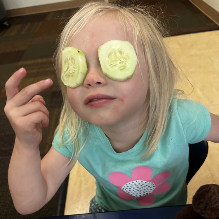 young girl at a lunch table with cucumbers on her eyes