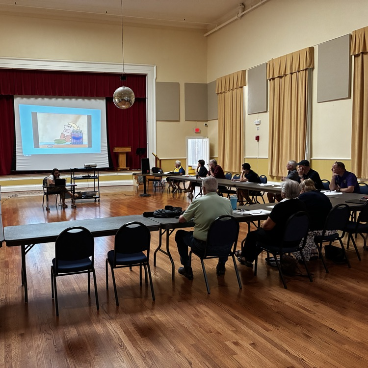 group of people sitting around tables, taking notes from the presentation