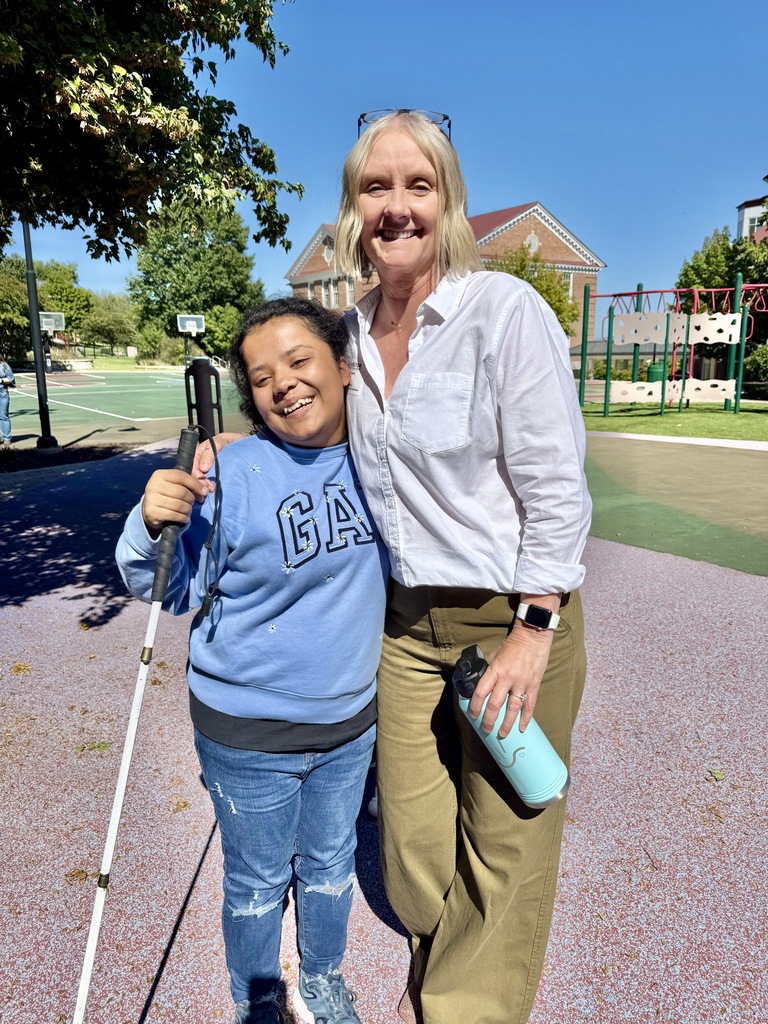 Kerry and female teenage student hugging. They are standing outside near the playground. 