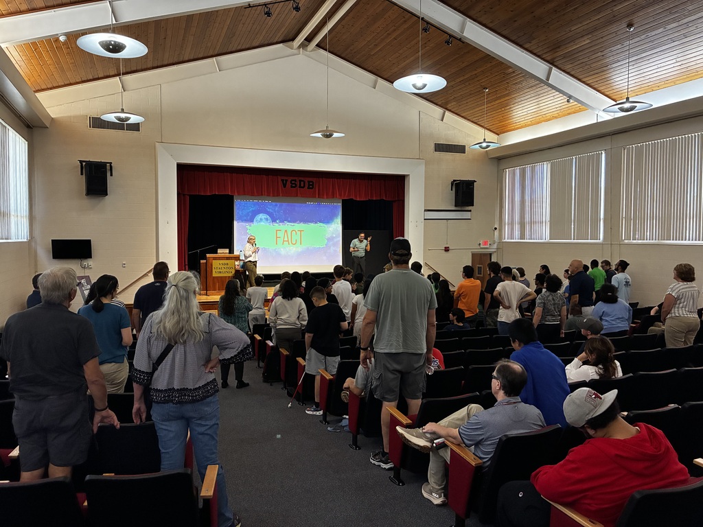 large group in the auditorium. Many people are standing, indicating they are "in" Kerry's trivia competition