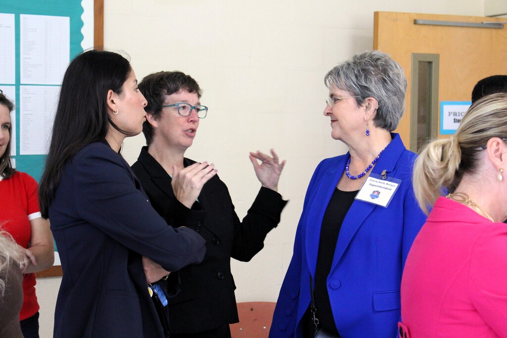 A group of women are talking indoors, an interpreter is mid sign. 