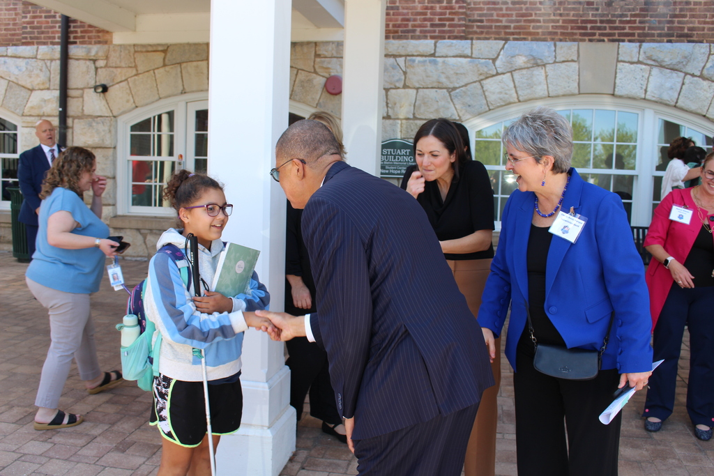 Dr. Jeffrey O. Smith shakes a young students hand. They are outside, and many people are walking around.