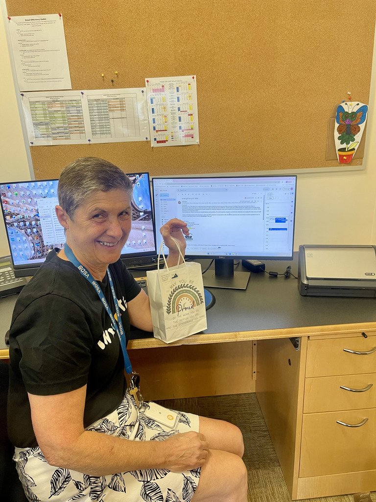 woman smiling at her desk while holding a goodie bag