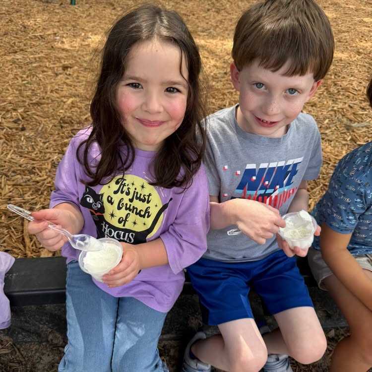 Three children sit on a bench, one with ice cream, another with yogurt, and the third with an unclear food.
