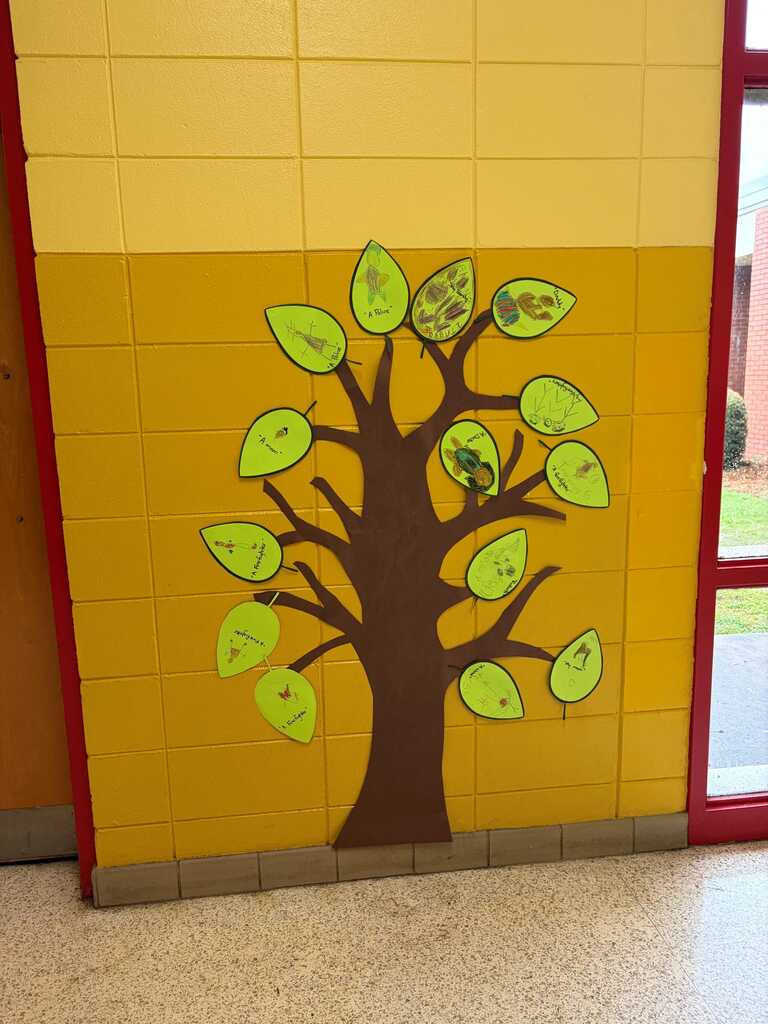 A yellow wall with a tree mural. The tree has green leaves and a brown trunk. The wall has a red border.