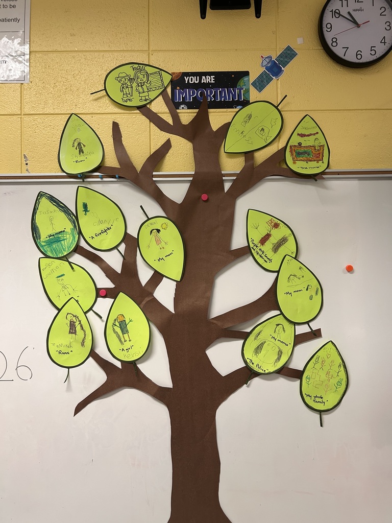 A tree with green leaves attached to a white board, a clock on the yellow wall, and a number "26" at the bottom.
