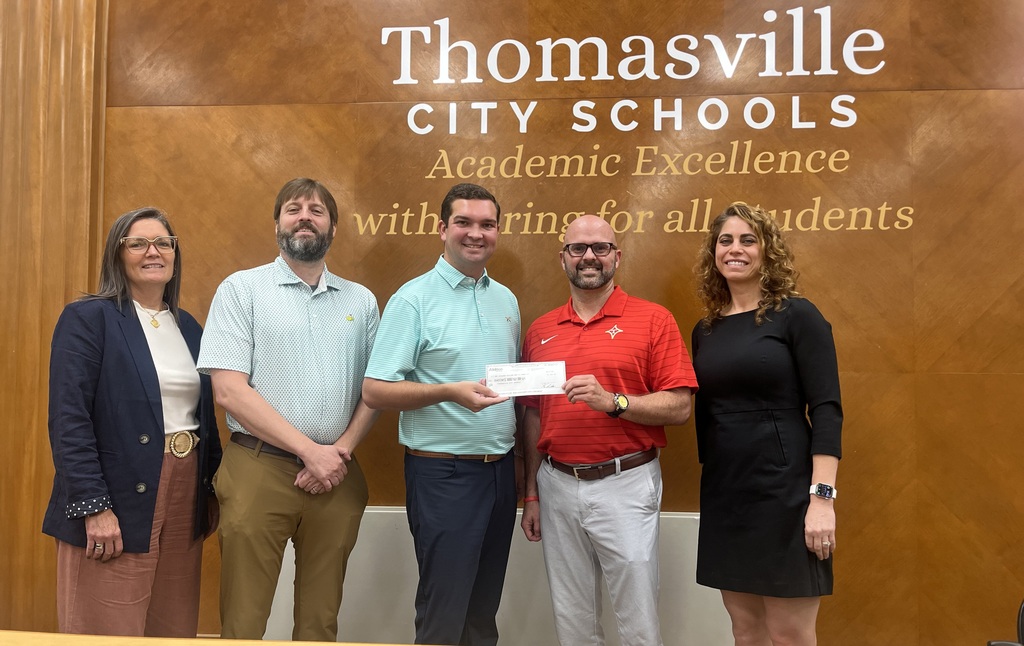 Five people stand in front of a sign for Thomasville City Schools. One holds a check.