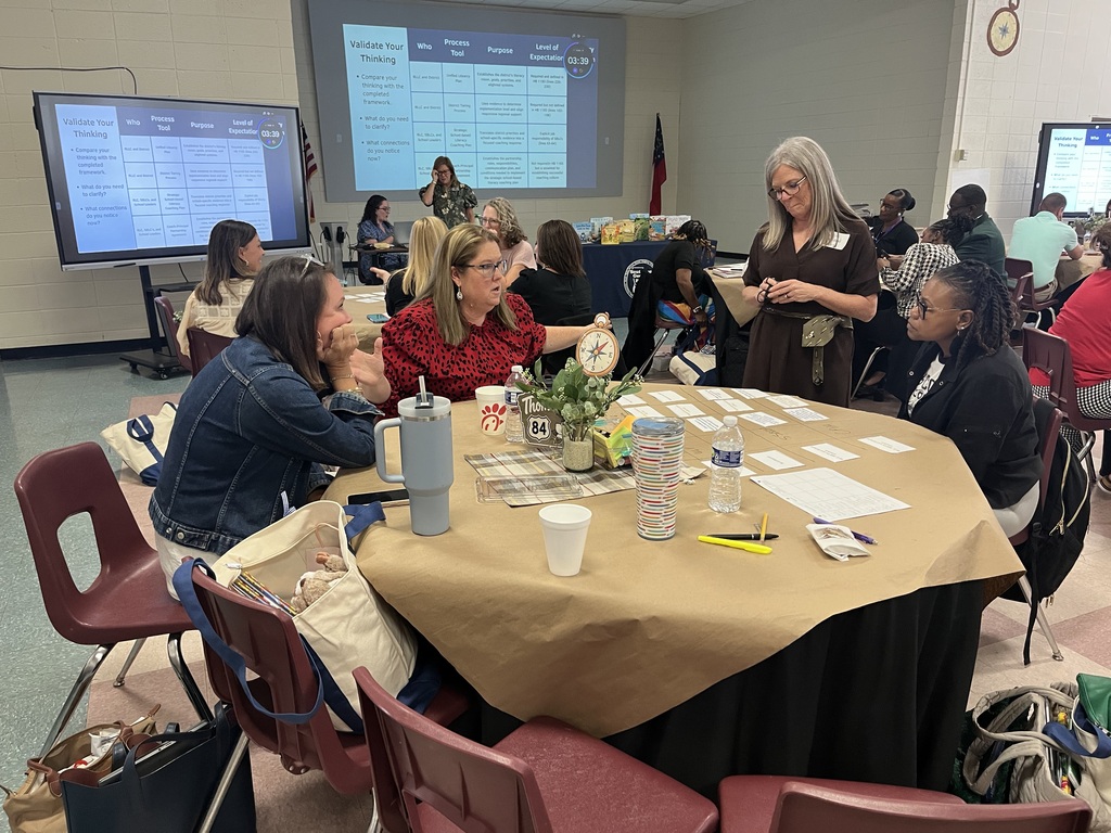A group of women in a classroom setting sitting around a table, with papers, cups, and bottles.