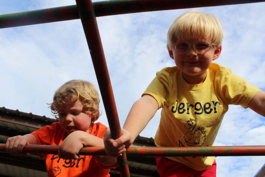 Two young boys on a play structure. One in yellow, the other in orange. They look at each other.
