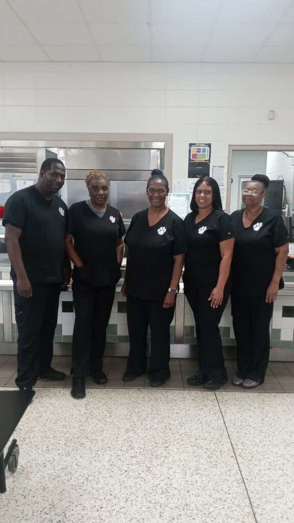 Five people in black uniforms stand together in a room with a white ceiling and floor.