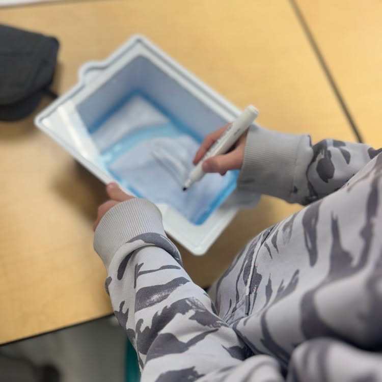 A person holds a stylus and draws on a tablet placed in a box on a desk.