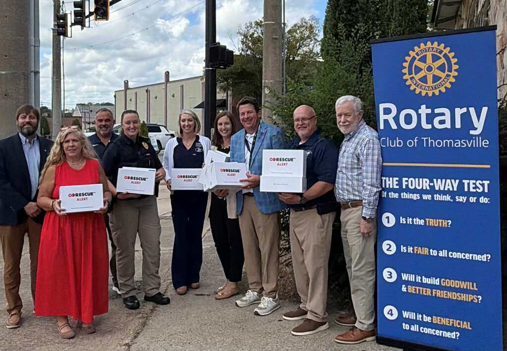 A group of people stand in front of a blue banner with Rotary Club of Thomasville text. They hold certificates.