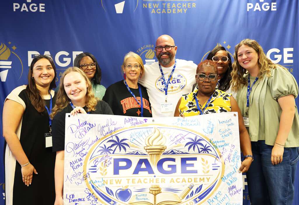 A group of people smile, posing behind a banner for PAGE New Teacher Academy. They hold a sign.