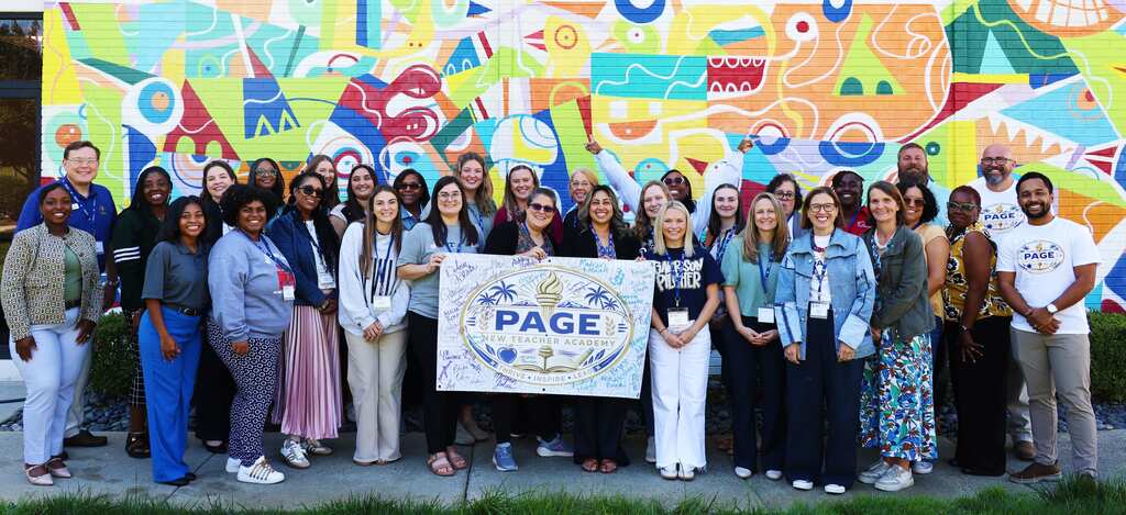 A group of people stands in front of a colorful mural, holding a white banner.