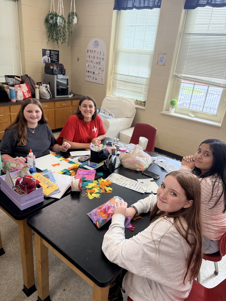Four girls seated around a table, engaged in an activity with colorful paper and crafts.