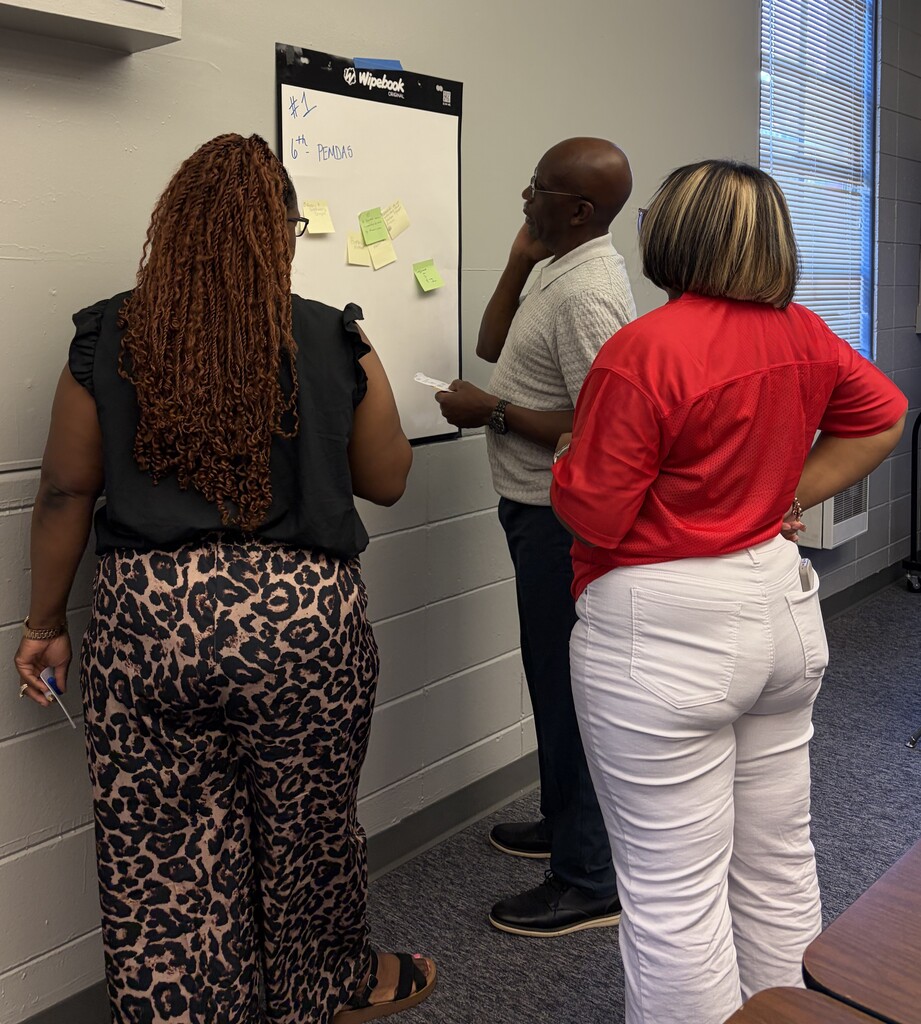 Three people face a whiteboard with sticky notes on it in a classroom.