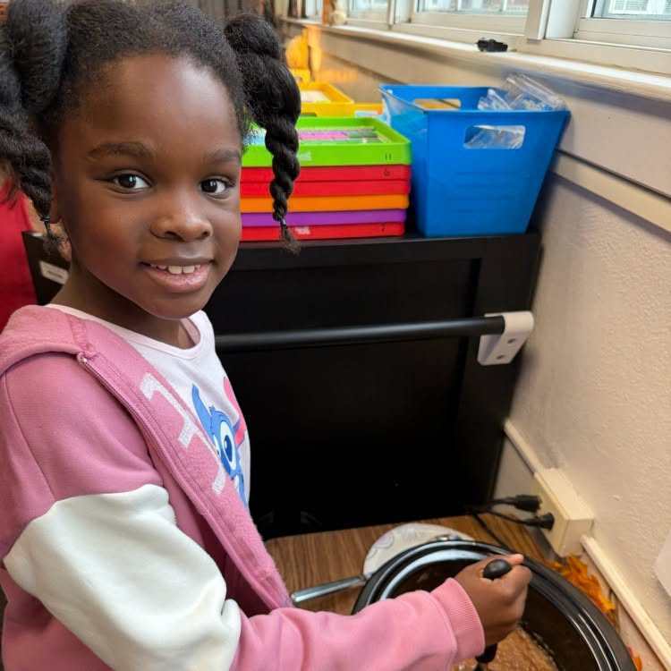 A girl with pigtails is holding a toy with wheels while sitting on a chair.