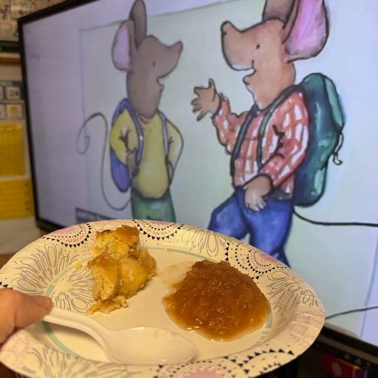 A person holds a plate with food in front of a TV screen showing two animated mice.