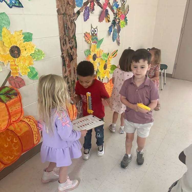 Four children standing in a room, two holding musical instruments, one holding a small object.
