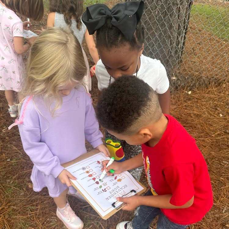 Kids look at a clipboard with paper and markers; one holds the clipboard, while the other holds a marker.