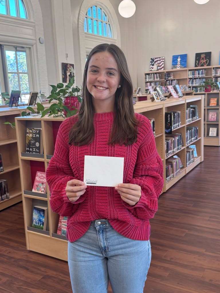 Woman holding white paper in a library with shelves full of books behind her.