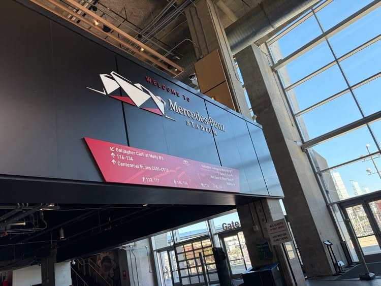 A modern building with a red banner has a logo and large windows; sunlight illuminates the interior.