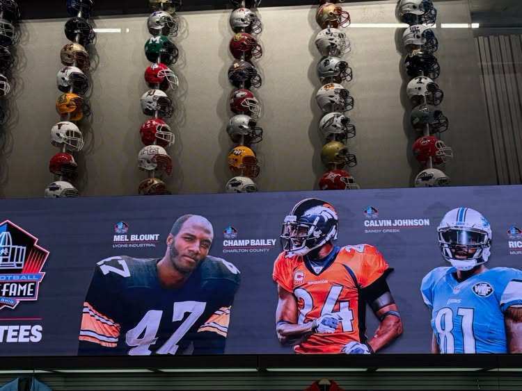 Helmets displayed on wall, a large screen shows three football players with numbers 47, 24, and 81.
