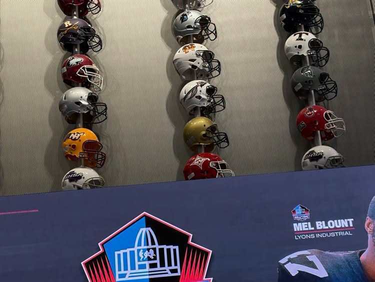 Helmets displayed on wall with logo and man's profile in lower right corner.