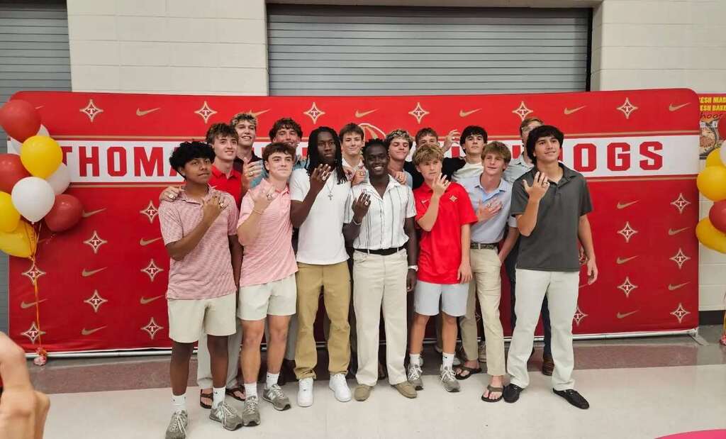 Group of students standing in front of a red backdrop with text and balloons.