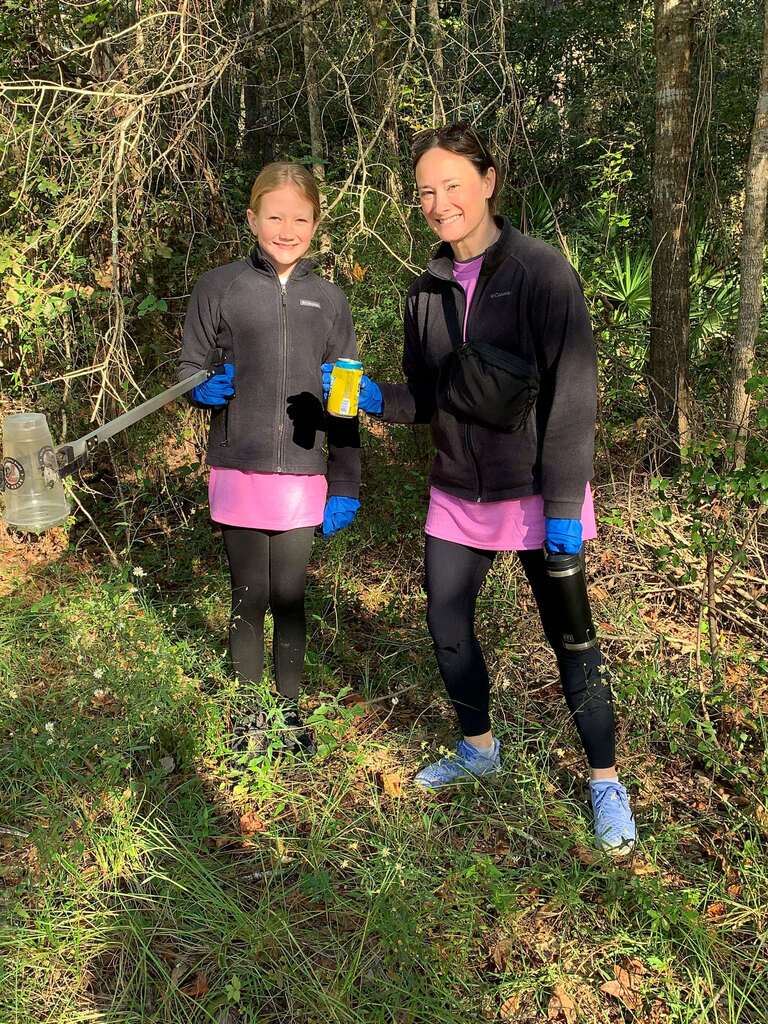 Two people in a forest, holding yellow object, one with gloves and a knee brace, other with gloves.