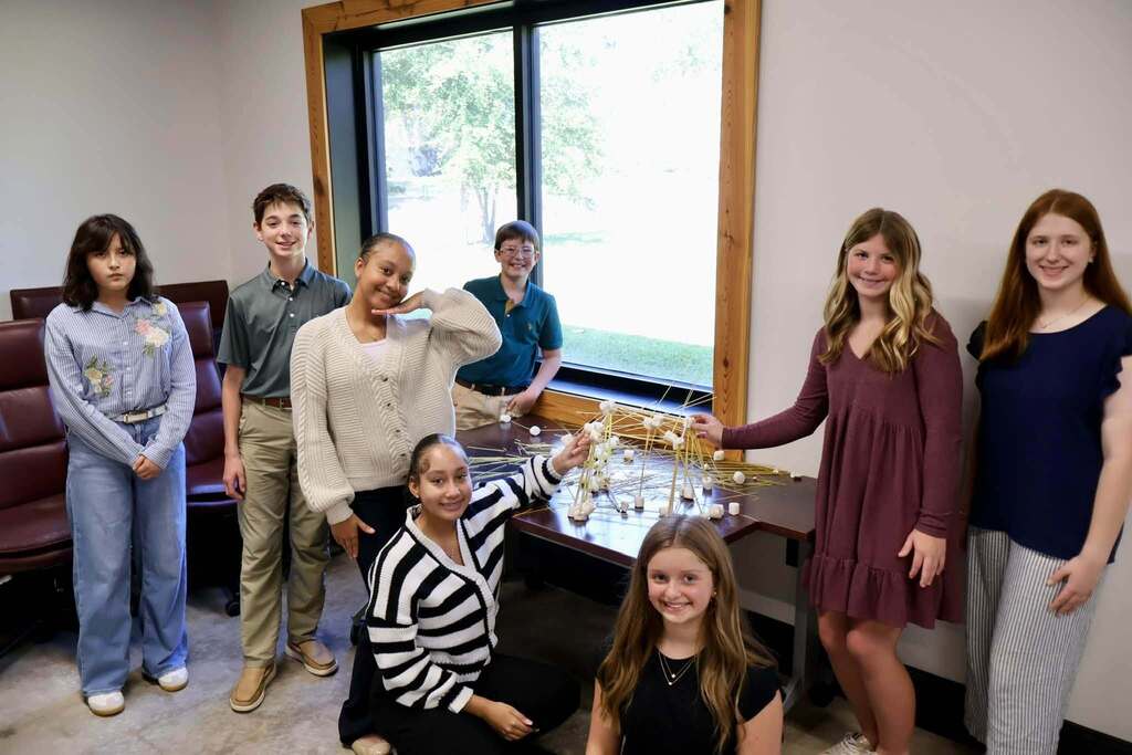 Students participating in the 2026–2027 Emerging Young Leaders Program pose around a conference table displaying a large spaghetti and marshmallow tower. Several students stand behind the table while others kneel in front, showcasing their teamwork during the kickoff event hosted by the Tifton-Tift County Chamber of Commerce.
