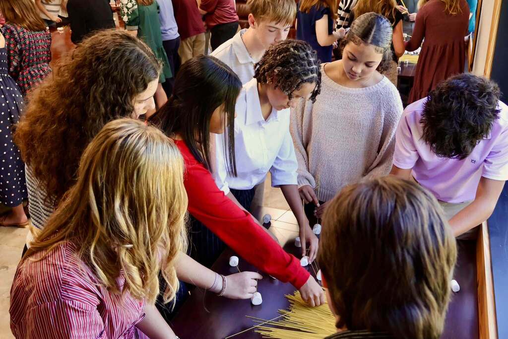 Students participating in the 2026–2027 Emerging Young Leaders Program work together around a conference table, using uncooked spaghetti and marshmallows to construct a tower during the kickoff event hosted by the Tifton-Tift County Chamber of Commerce. The hands-on challenge encourages teamwork, communication, and problem-solving skills.