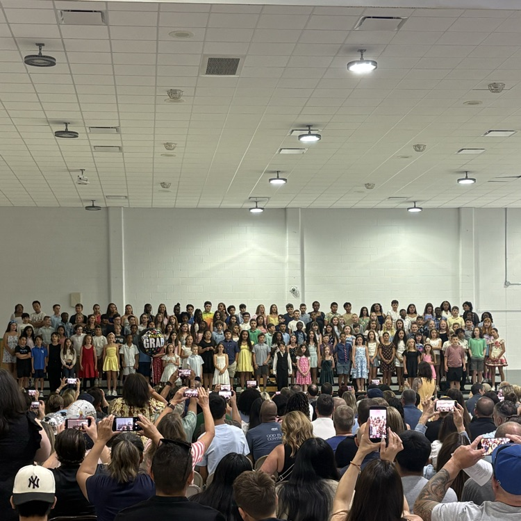 students standing on risers on a stage singing a song 