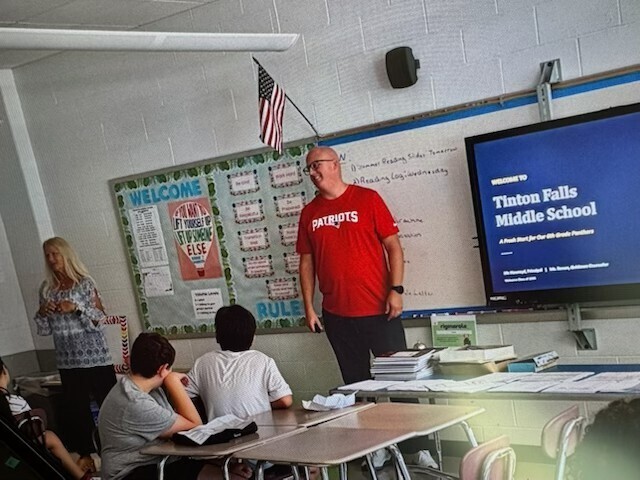 Mr. Howroyd and Ms. Ronan in front of a classroom with a presentation featured on the screen