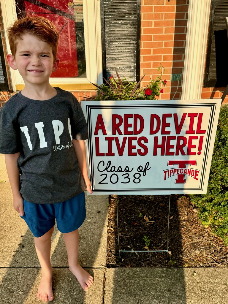 Kindergarten student standing with the yard sign saying A Red Devil Lives Here!
