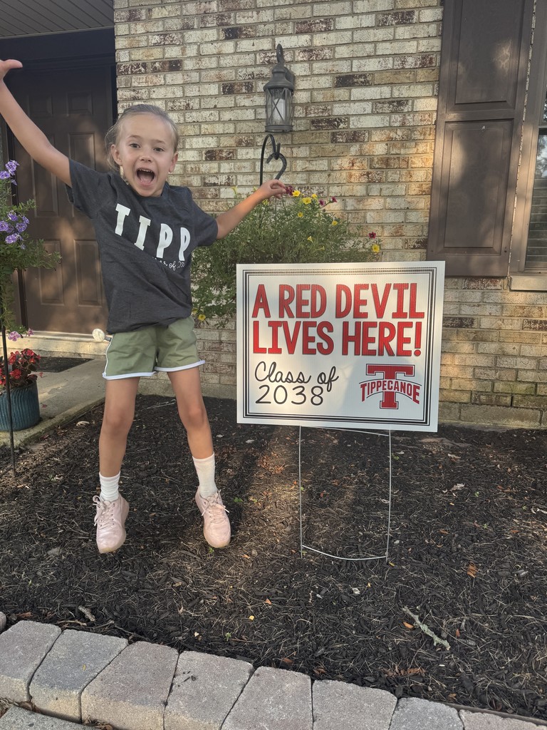Kindergarten student standing with the yard sign saying A Red Devil Lives Here!